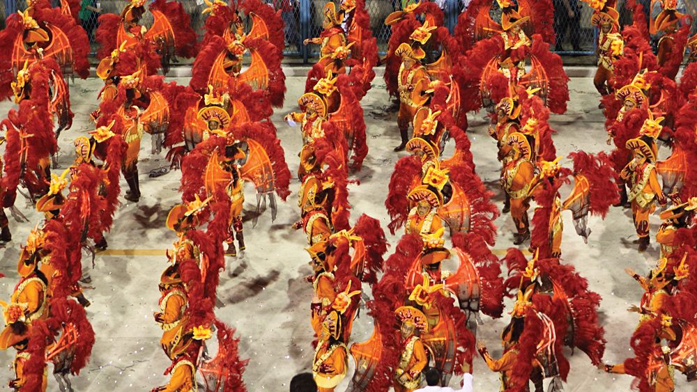 Danseurs en costumes de plumes rouges et orangées défilant au Sambodrome de Rio