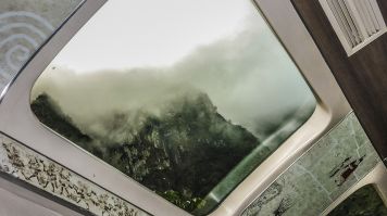 Montagnes couvertes de nuages vues à travers une fenêtre de toit d’un train panoramique vers le Machu Picchu