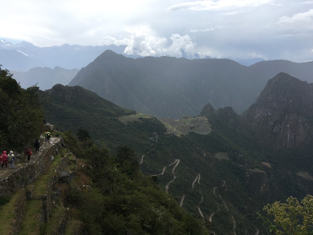 Randonneurs sur le Chemin de l’Inca près de la porte du Soleil, avec le Machu Picchu et la route en lacets en contrebas
