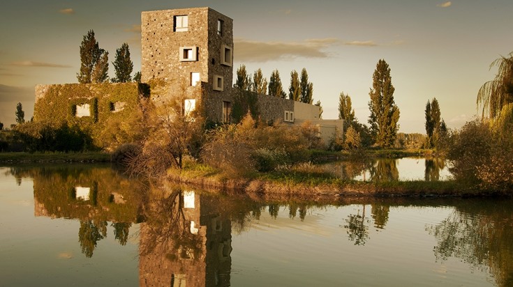 Bâtiment en pierre d’une bodega se reflétant dans un bassin, entouré d’arbres aux couleurs d’automne