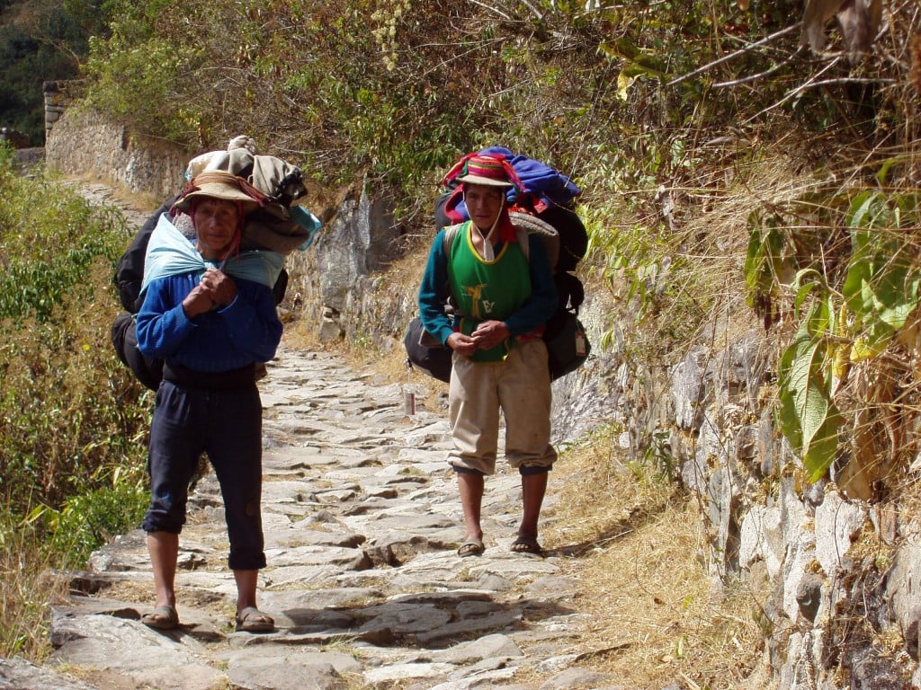 Deux porteurs andins chargés de sacs sur un sentier pavé du Chemin de l’Inca