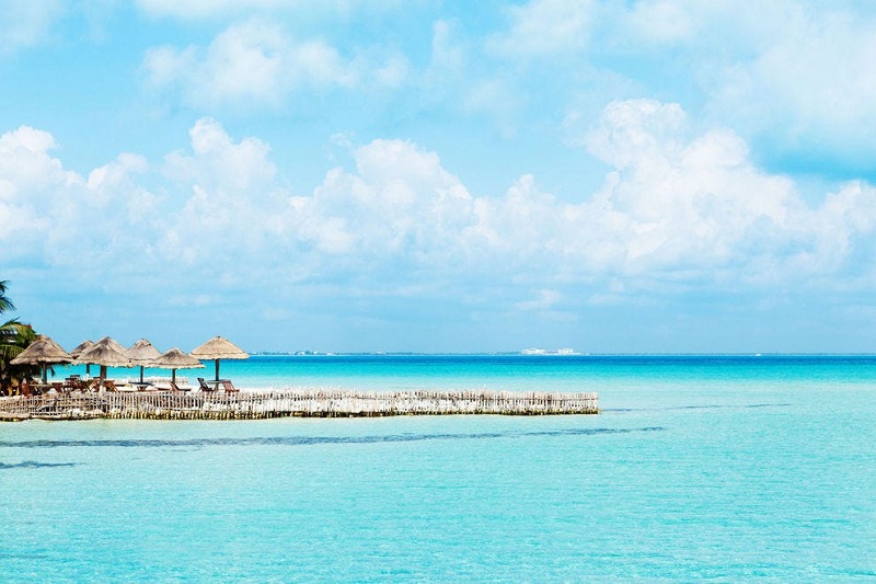 Eau turquoise peu profonde et paillotes au bord de la plage d’Isla Mujeres