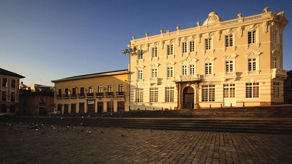 Palais colonial blanc et maisons à balcons sur une place pavée du centre historique de Quito