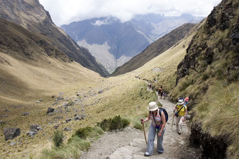 Randonneurs gravissant le sentier du Chemin de l’Inca dans une haute vallée andine, en direction du col de Warmiwañusca